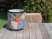 A multicolored round ceramic flower pot with floral patterns, placed on a wooden surface with a backdrop of greenery.