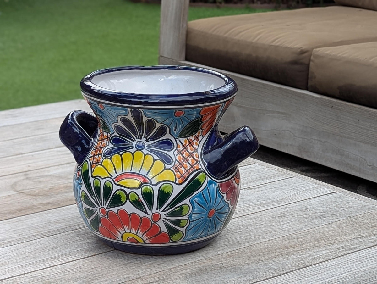 A colorful round Talavera ceramic flower pot with handles, featuring a floral pattern, placed on a wooden surface.