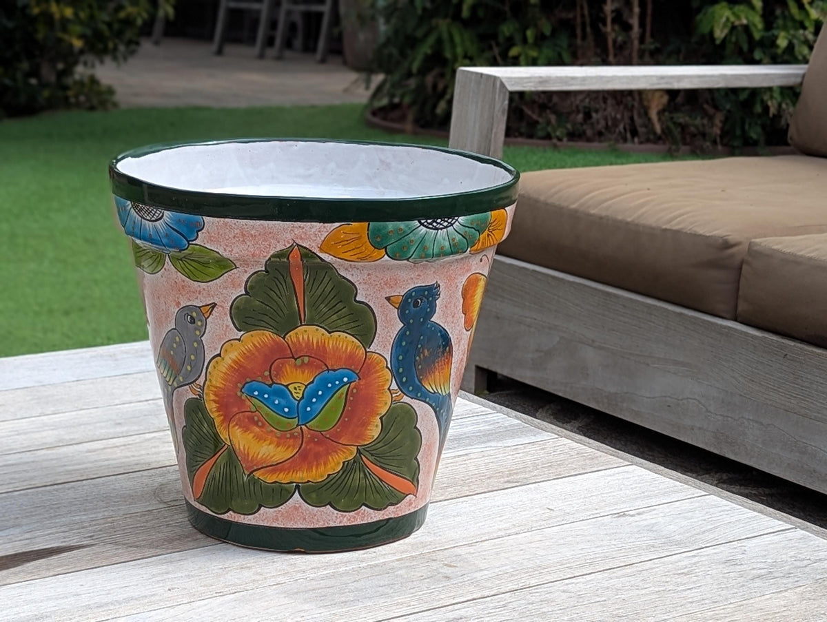 A multicolored round ceramic planter with a floral pattern, placed on a wooden surface with outdoor furniture in the background.
