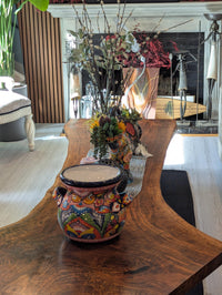 A colorful Talavera ceramic round flower pot with blue trim and handles, displayed indoors.
