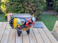 A hand-painted Talavera ceramic planter in the shape of a blowfish with a colorful and decorative design, placed on a wooden surface outdoors.