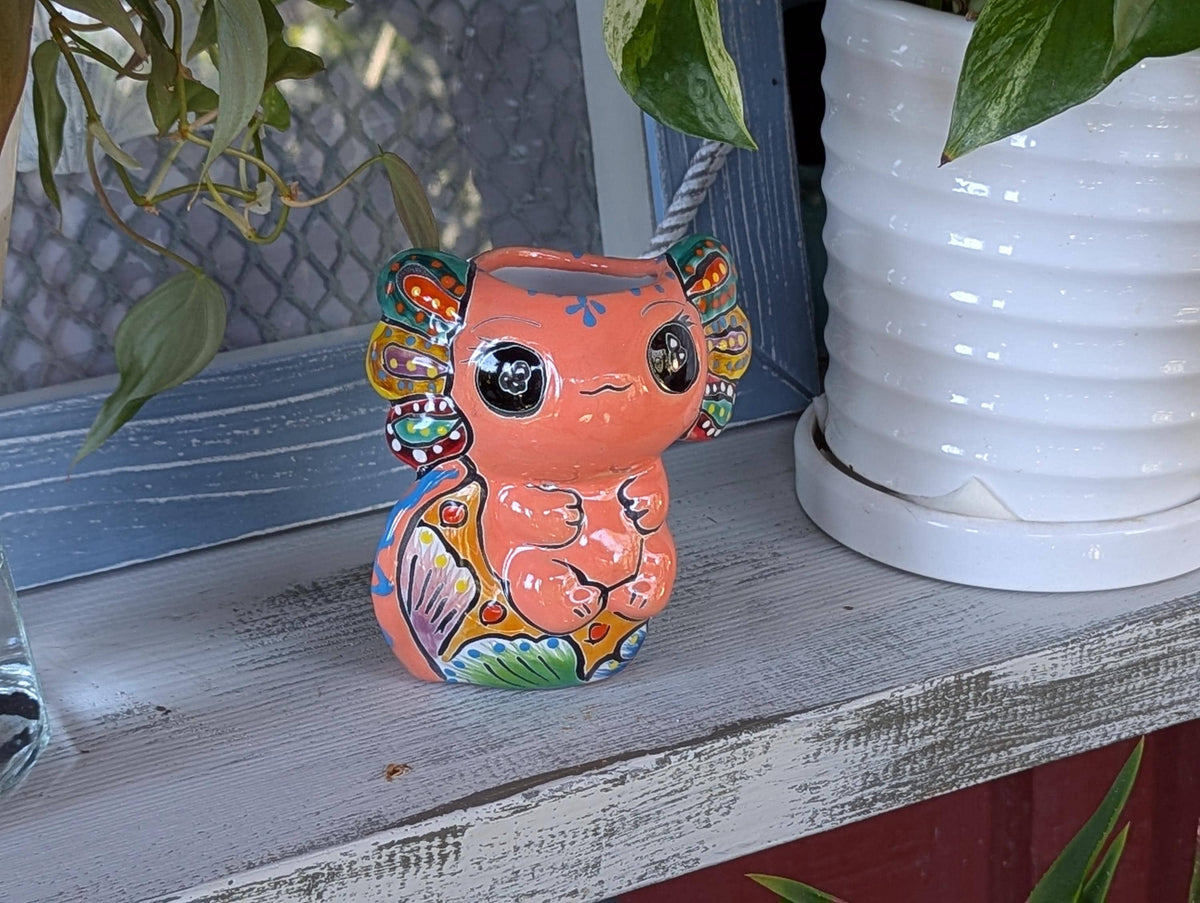 A ceramic planter in the shape of an axolotl salamander with a pink body, green ears, and a multicolored pattern.