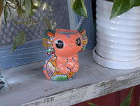 A ceramic planter in the shape of an axolotl salamander with a pink body, green ears, and a multicolored pattern.