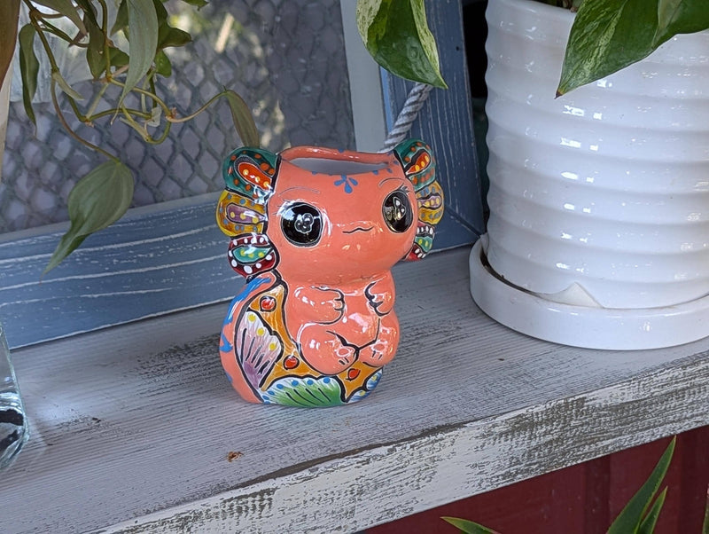 A ceramic planter in the shape of an axolotl salamander with a pink body, green ears, and a multicolored pattern.