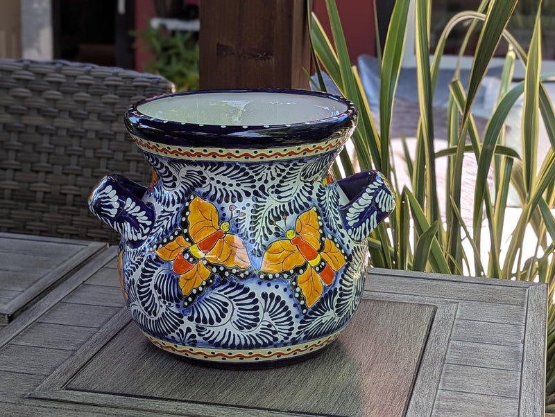 A round, ceramic Talavera planter with blue trim and handles, featuring a floral pattern with yellow and dark blue colors.
