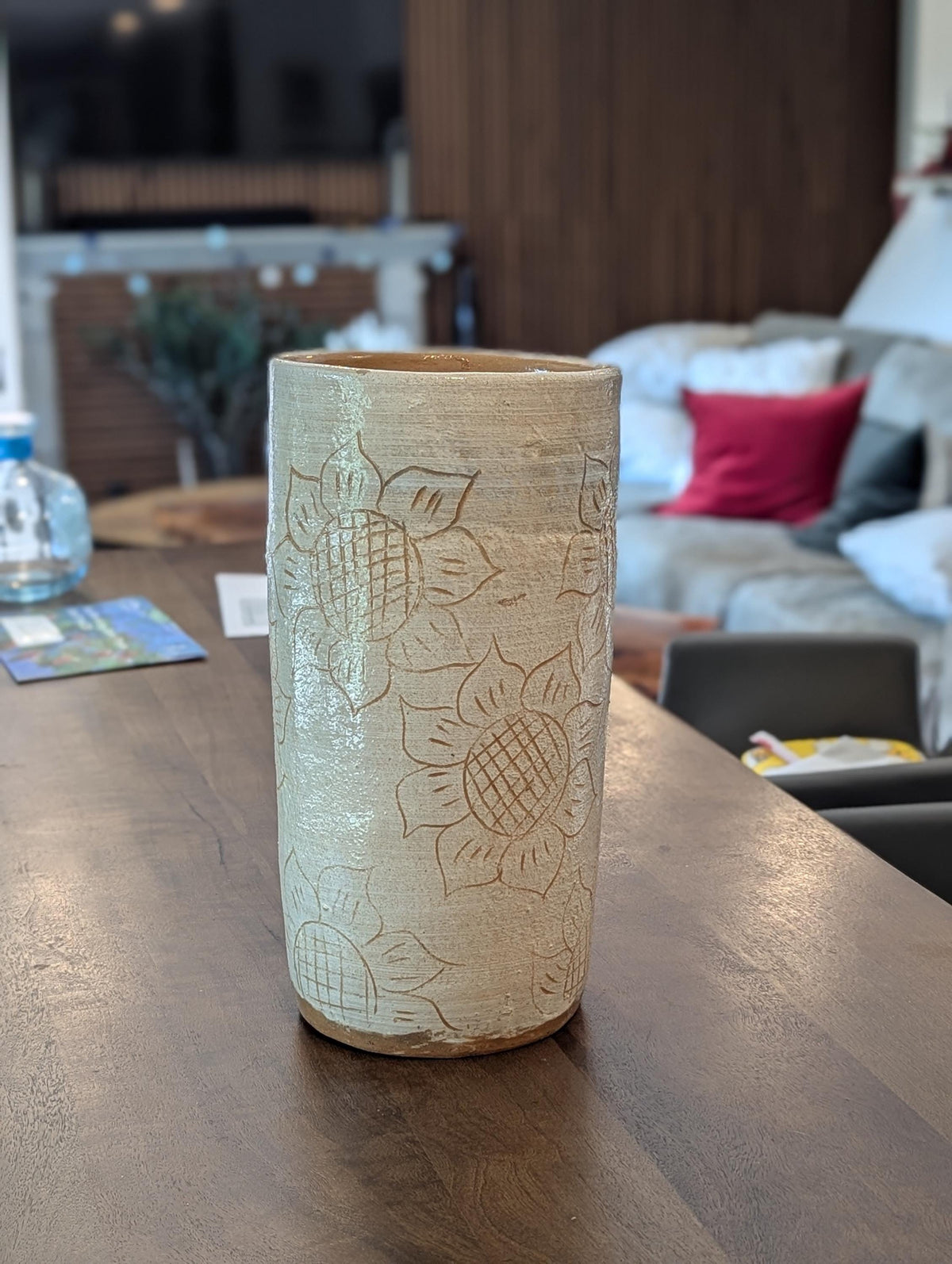 Cylindrical ceramic vase with sunflower patterns on a wooden table in a living room setting.