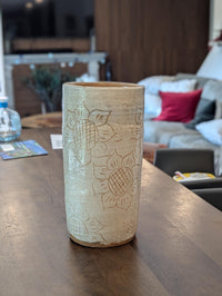 Cylindrical ceramic vase with sunflower patterns on a wooden table in a living room setting.