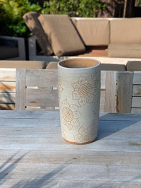 Cylindrical ceramic vase with sunflower design on a wooden table outdoors