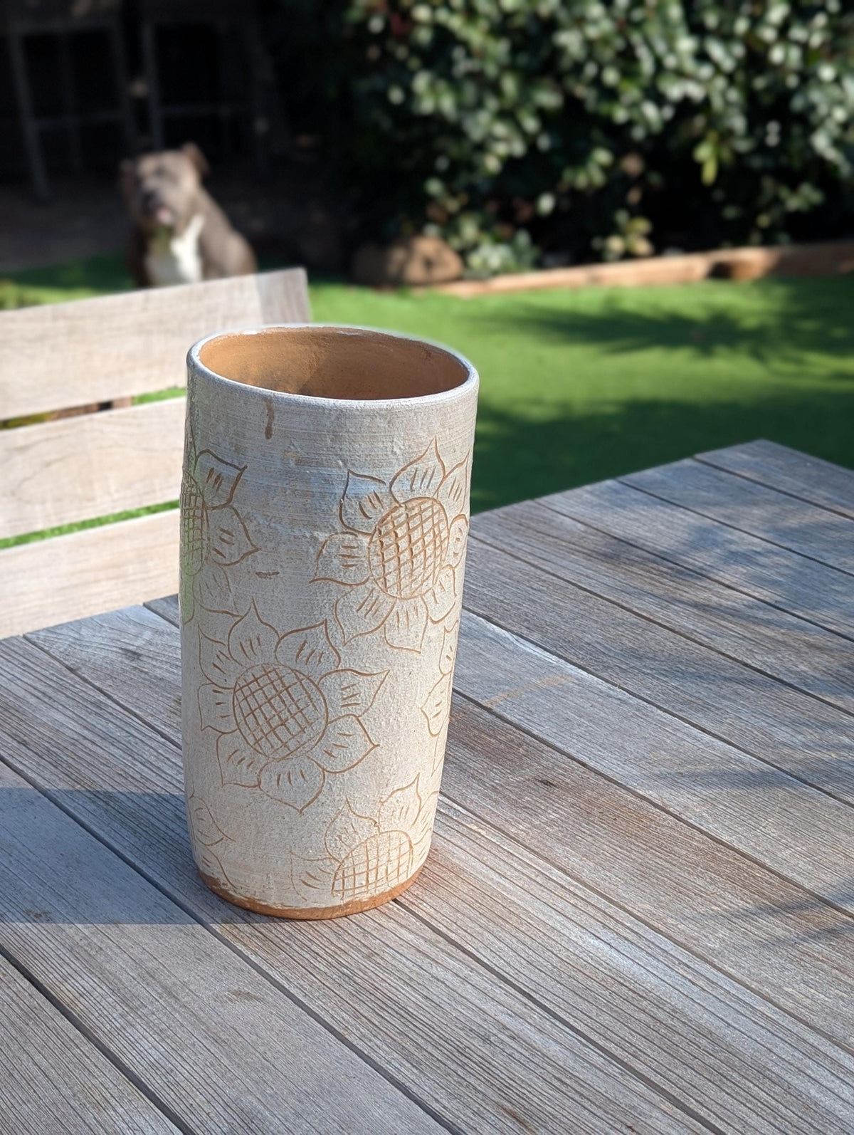 Cylindrical ceramic vase with embossed patterns on a wooden table outdoors