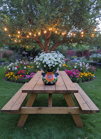 Wooden picnic table under a tree with string lights in a garden setting.