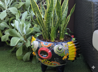 Colorful fish-shaped pot with a snake plant inside, surrounded by greenery.