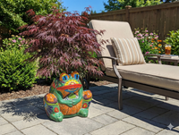 Colorful frog sculpture on a patio with a lounge chair and plants in the background