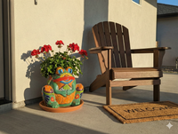 Colorful dragon-shaped planter with flowers on a patio next to a wooden chair and welcome mat.