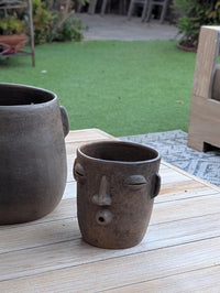 Ceramic face-shaped pot on a wooden surface with a garden background
