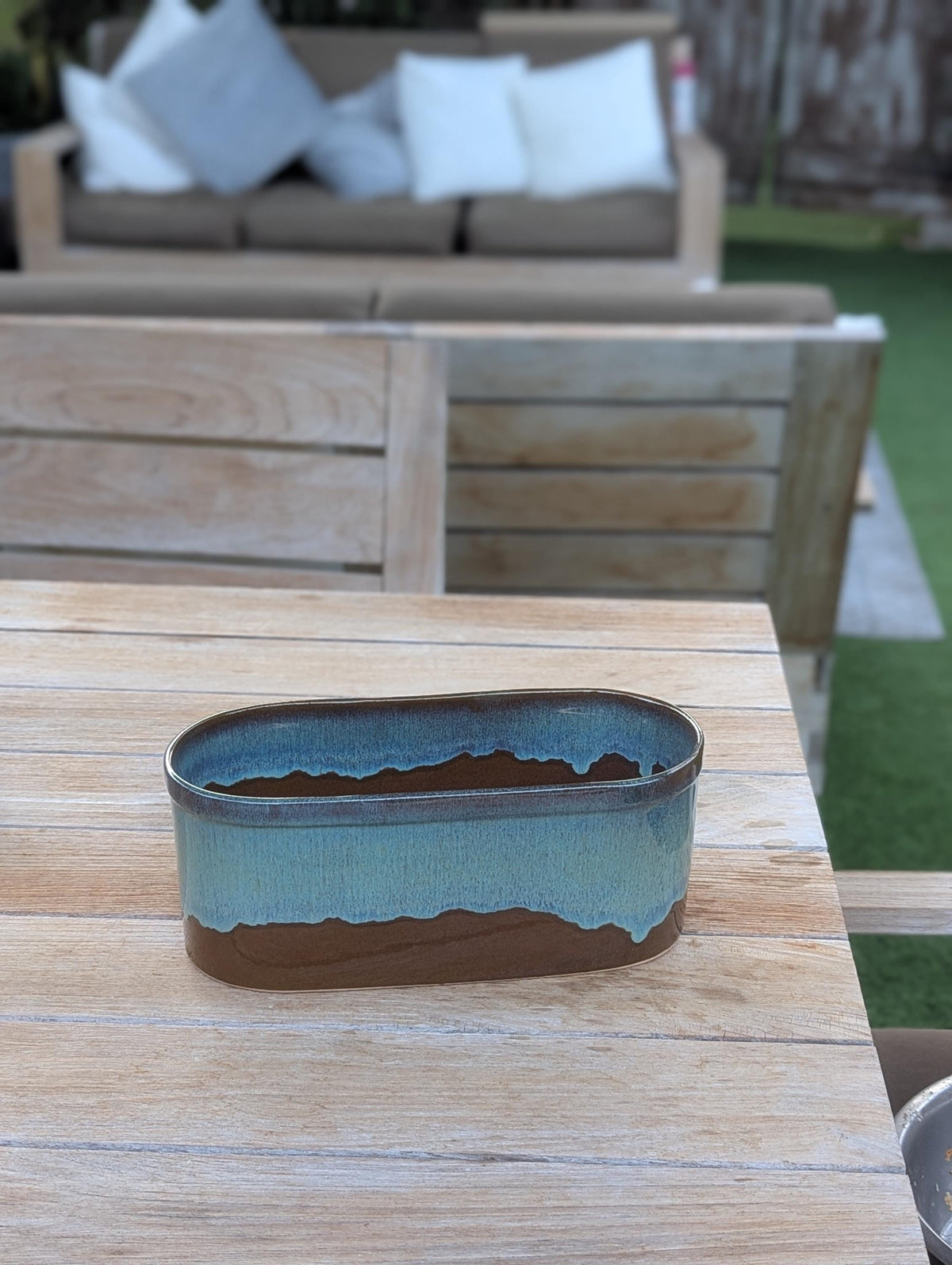 Ceramic planter with blue and brown design on a wooden table outdoors