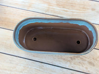 Brown ceramic planter with blue rim on a wooden surface