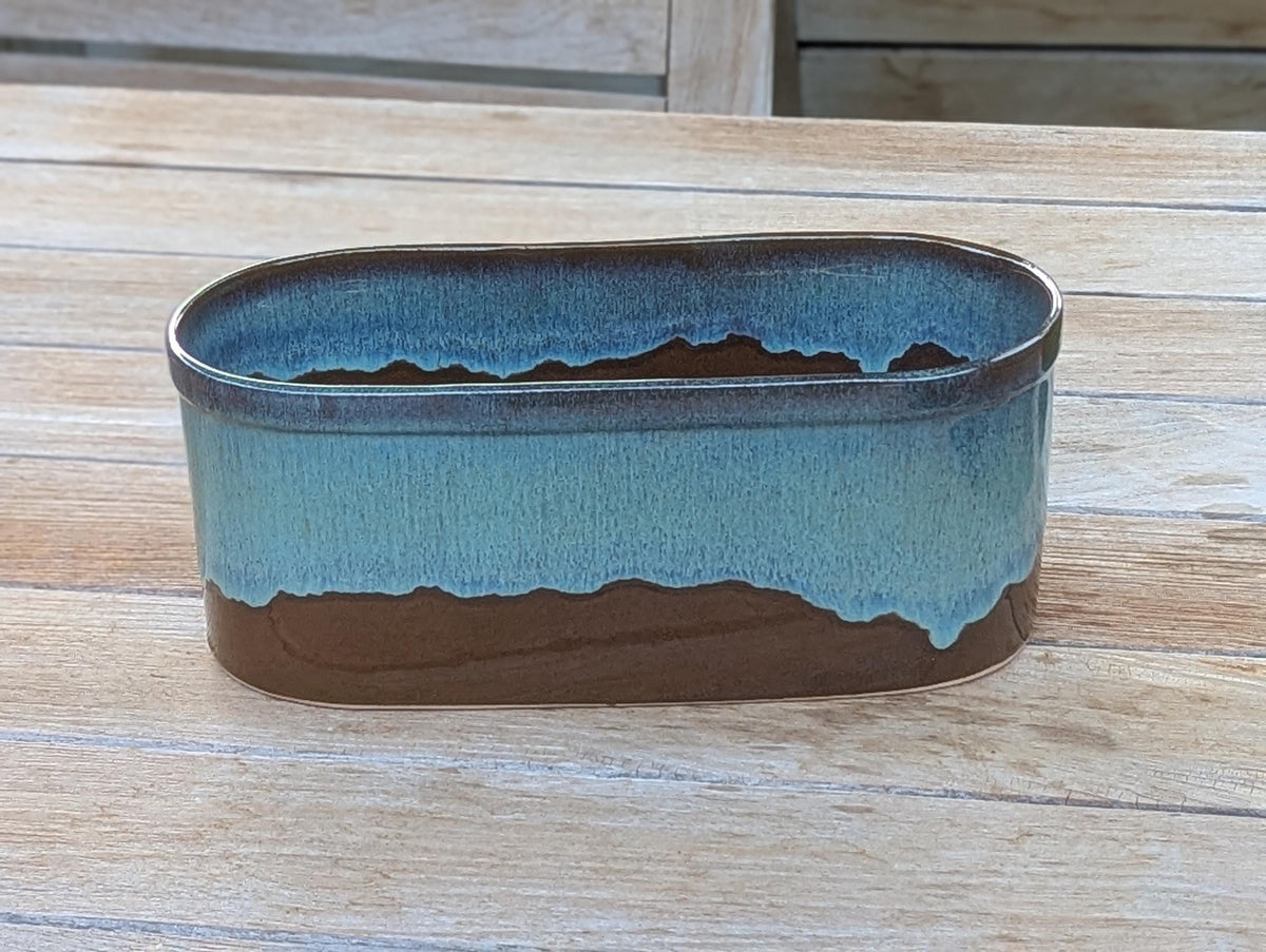 Oval ceramic planter with blue and brown glaze on a wooden surface