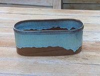 Oval ceramic planter with blue and brown glaze on a wooden surface