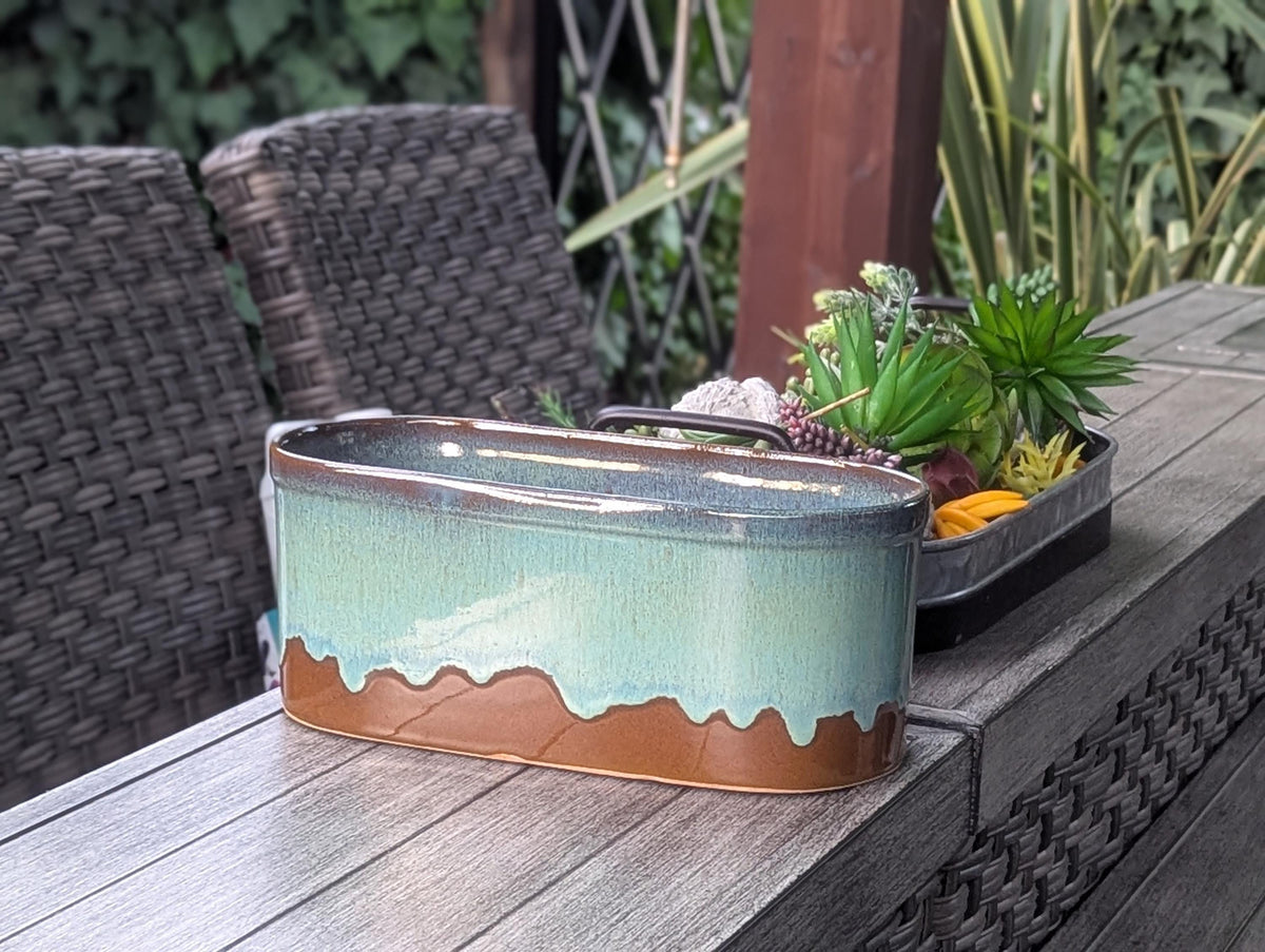 Decorative ceramic planter with succulents on a wooden table outdoors.