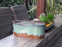 Decorative ceramic planter with succulents on a wooden table outdoors.