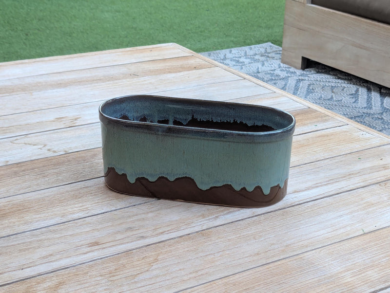 Oval-shaped planter with a green and brown gradient on a wooden surface.
